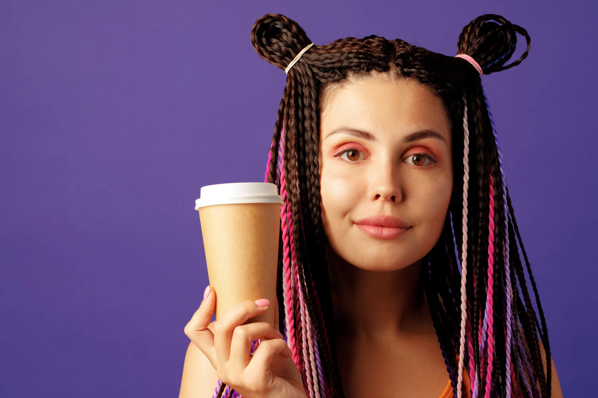 Young caucasian woman with colorful long cornrows holding a cup of coffee against purple background